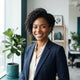 A smiling diverse woman posing for a professional portrait in a bright, modern office setting with teal-toned decor.