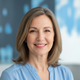A happy woman in her 50s smiles gently, her healthy, smooth skin visible, against a blurred background of slate blue and brig