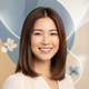A smiling woman in her late 20s with styled, straight hair looks confidently at the camera, conveying satisfaction.